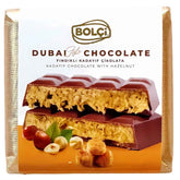 A 100g package of Bolci Dubai Kadayif Chocolate with Hazelnut, showing the chocolate bar filled with creamy filling and whole hazelnuts in front of the Bolci packaging.